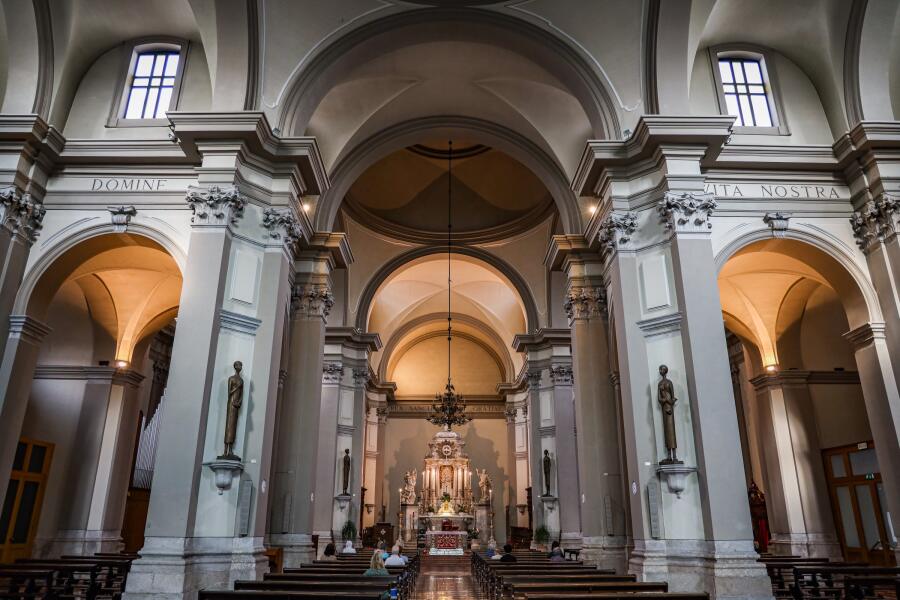 A church interior with tall plaster arches and statues flanking the nave, lit from clerestory windows.