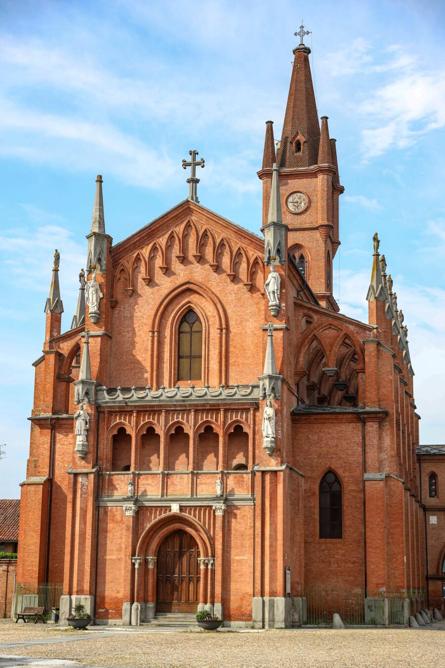 A red brick church facade with a rose window and a tall clock tower against a bright blue sky.