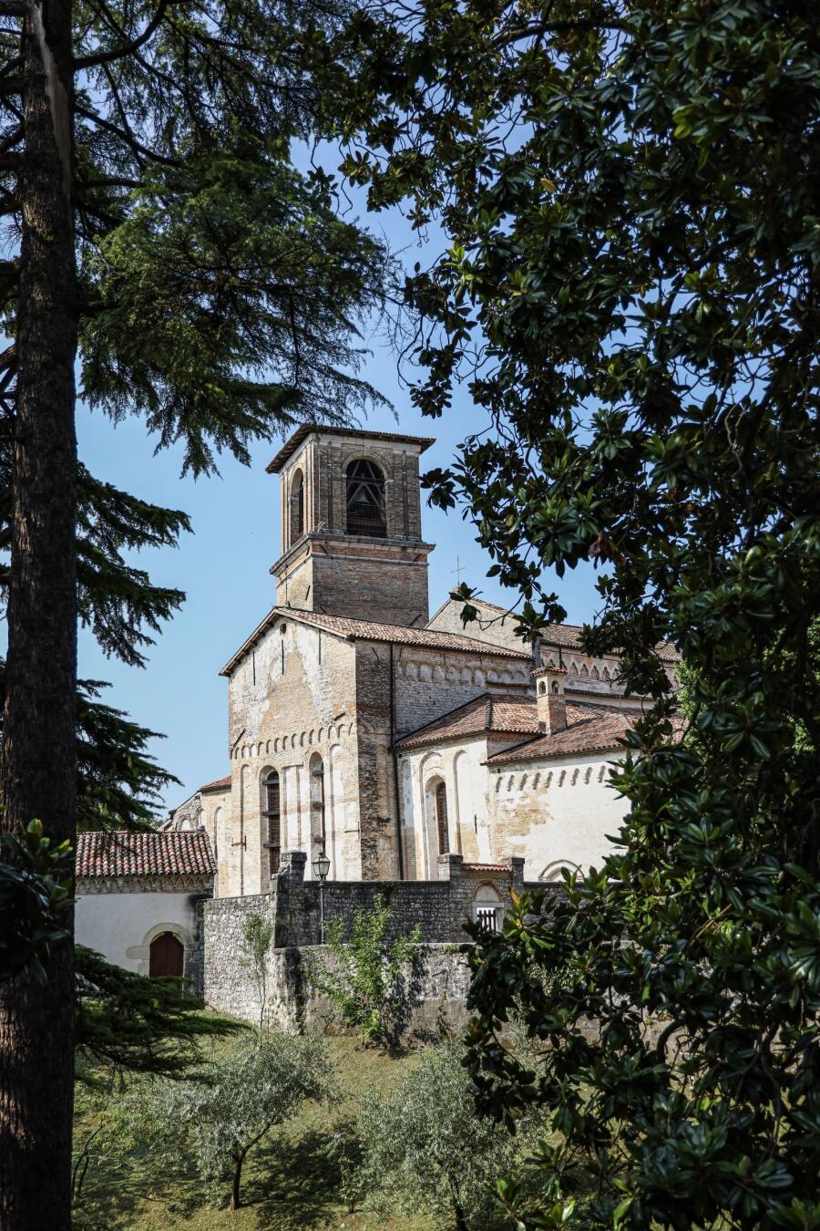A stone church and bell tower on a rise, partly screened by dark foliage in the foreground.