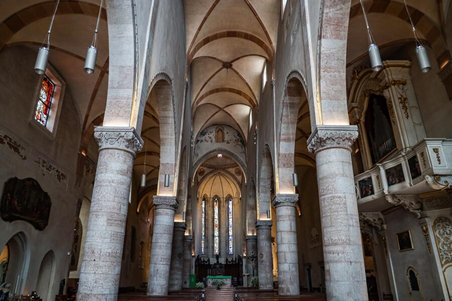 Massive round stone columns marching down a gothic church interior toward a lit apse.