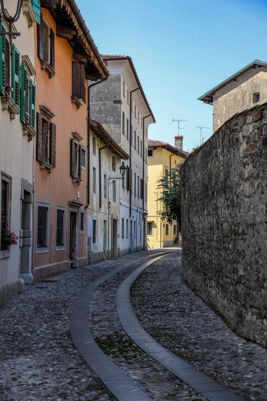 A cobbled lane curving between a long stone wall and a terrace of pastel houses.