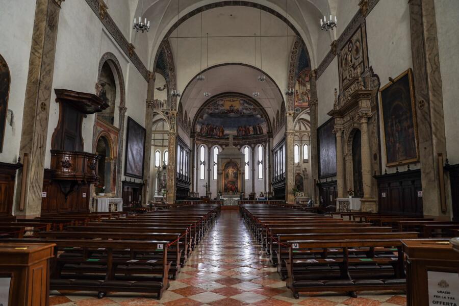 The nave of a basilica looking toward the altar, with dark wooden pews and a chequered marble floor.