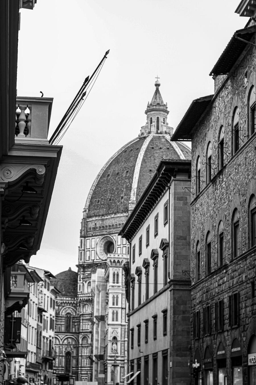 Black and white photograph looking up a narrow Florence street to the ribbed dome of the cathedral.