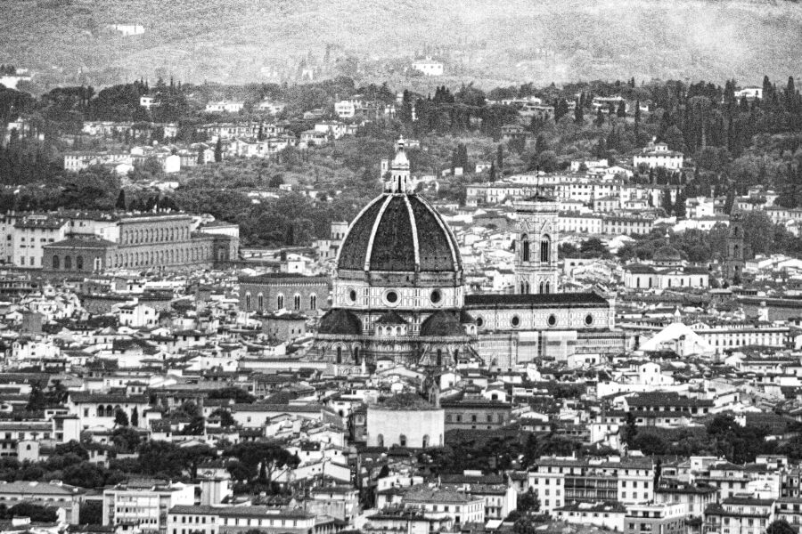 Black and white view across Florence rooftops to the dome and campanile of the cathedral, with hills behind.