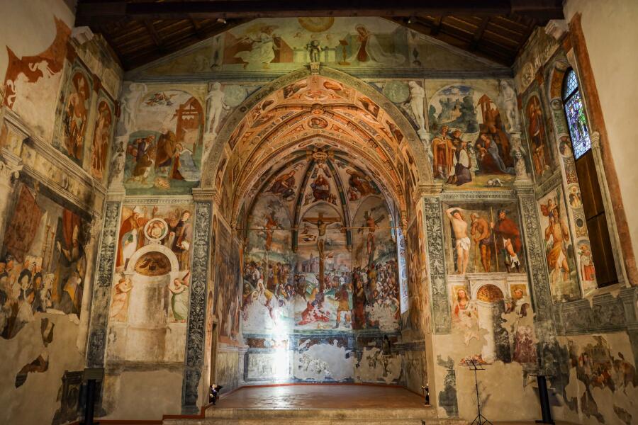 A small chapel covered floor to ceiling in faded frescoes, with a low arch over the altar.