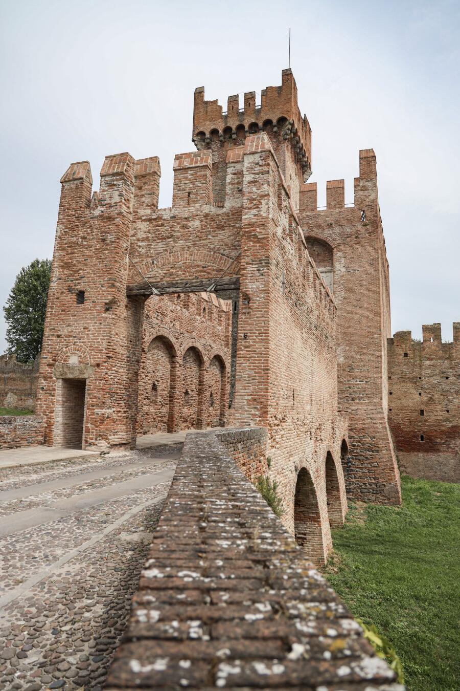 A crenellated brick gatehouse and curtain wall with a cobbled ramp leading up to the entrance.