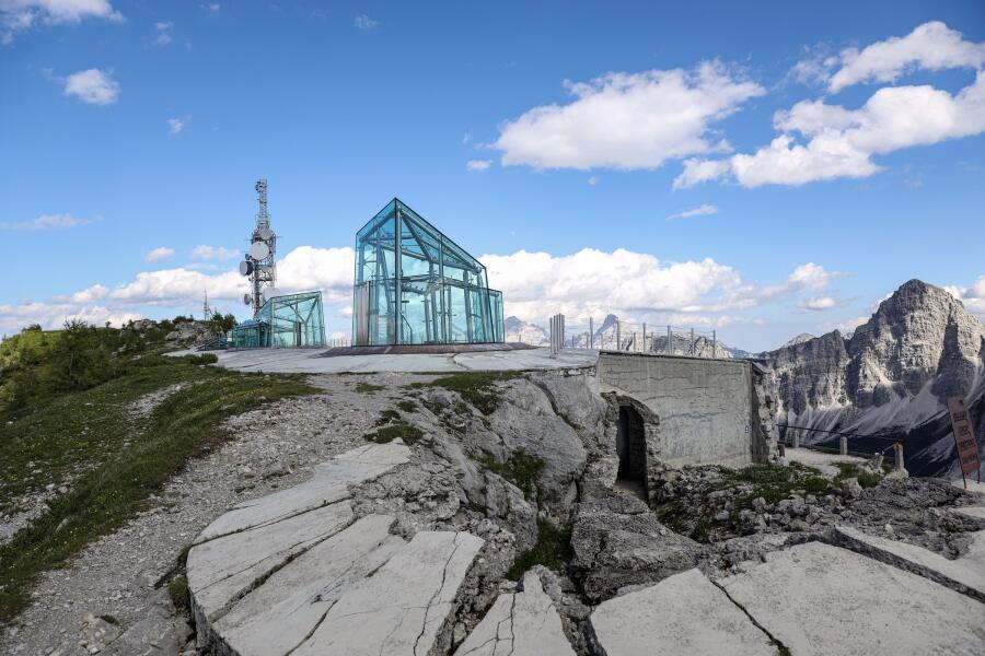 A modern glass and steel structure standing on a broken limestone plateau, with mountains behind it.