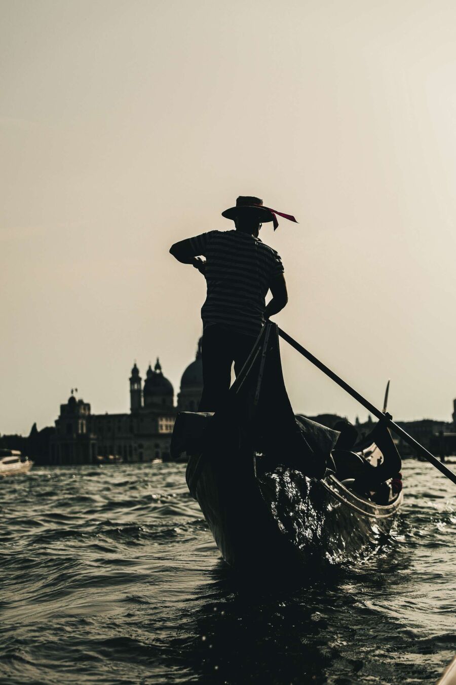 A gondolier silhouetted against pale water and a distant skyline, leaning into the oar.