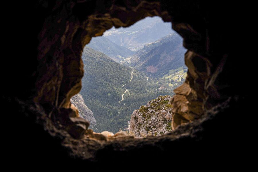 A valley seen through the rough circular opening of a rock tunnel, the stone edges dark against the light.
