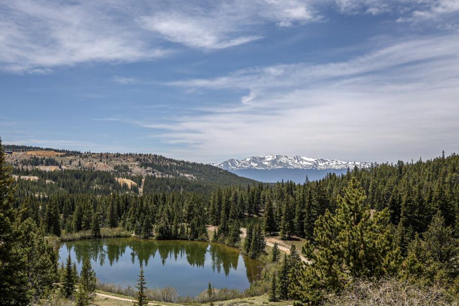 A small still lake ringed by conifers, with a snow dusted range along the far horizon.