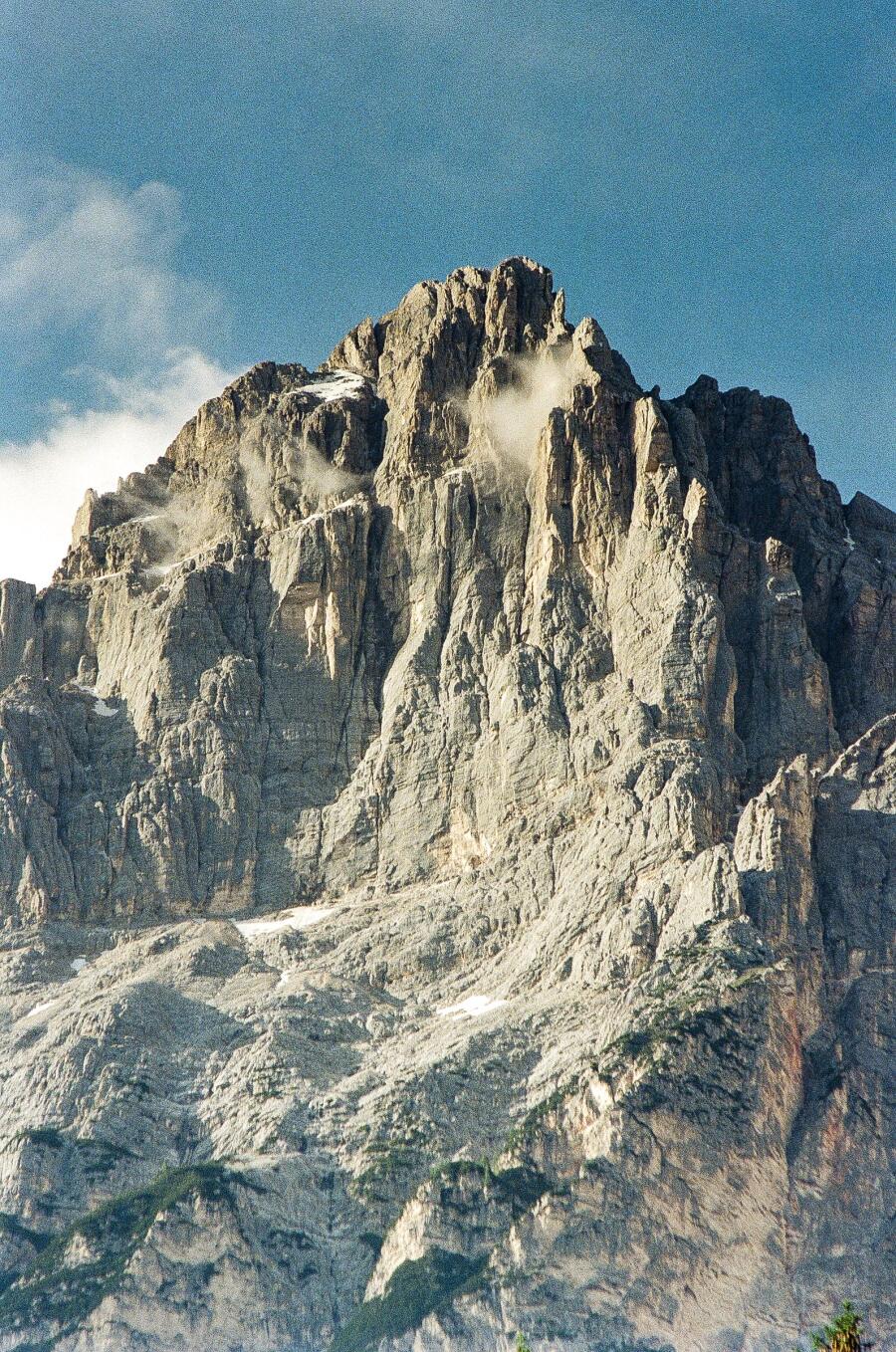 A steep limestone peak rising into cloud above a scree slope.