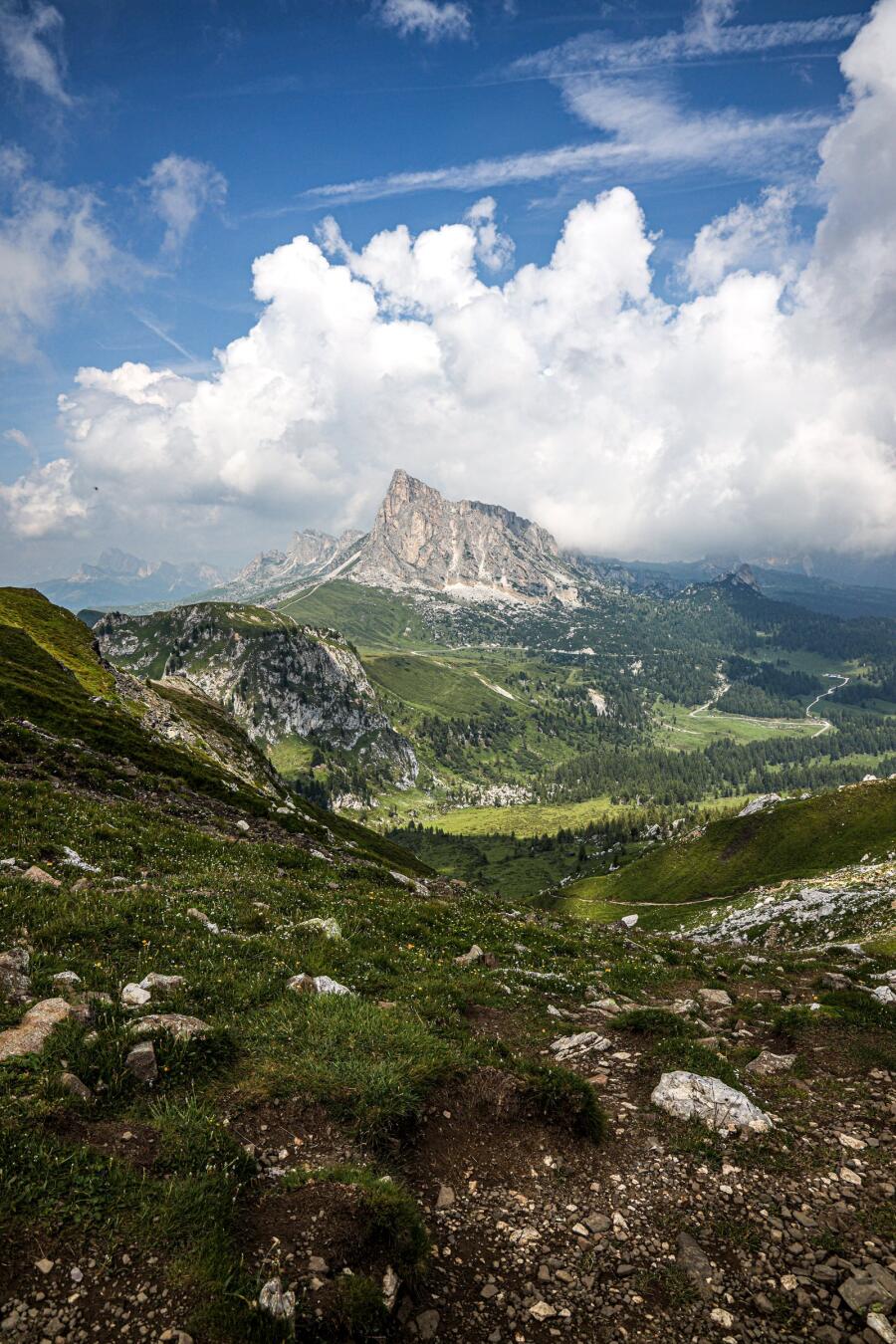 A single pyramid shaped peak seen across a wide green meadow under piled cloud.