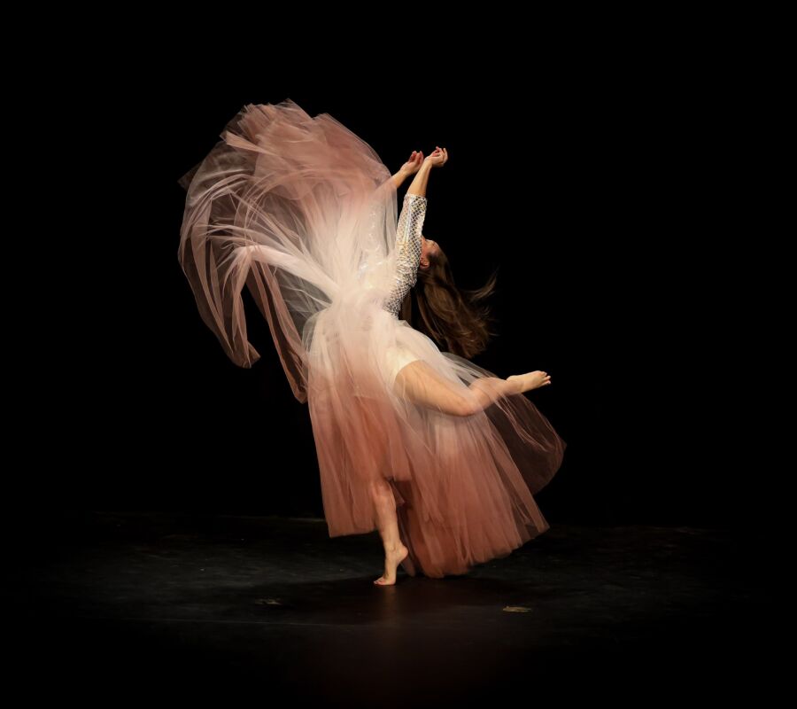 A dancer in a pale pink skirt spinning against a black stage, the fabric flaring out into a wide arc.