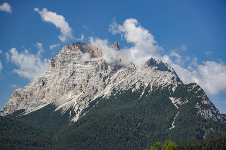 A layered limestone peak streaked with snow along its ledges, half wrapped in cloud.