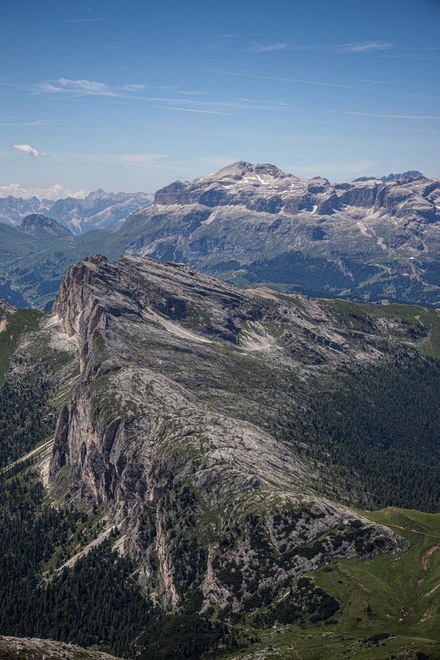 A forested spur of rock projecting into a wide valley, with a hazy range on the horizon.