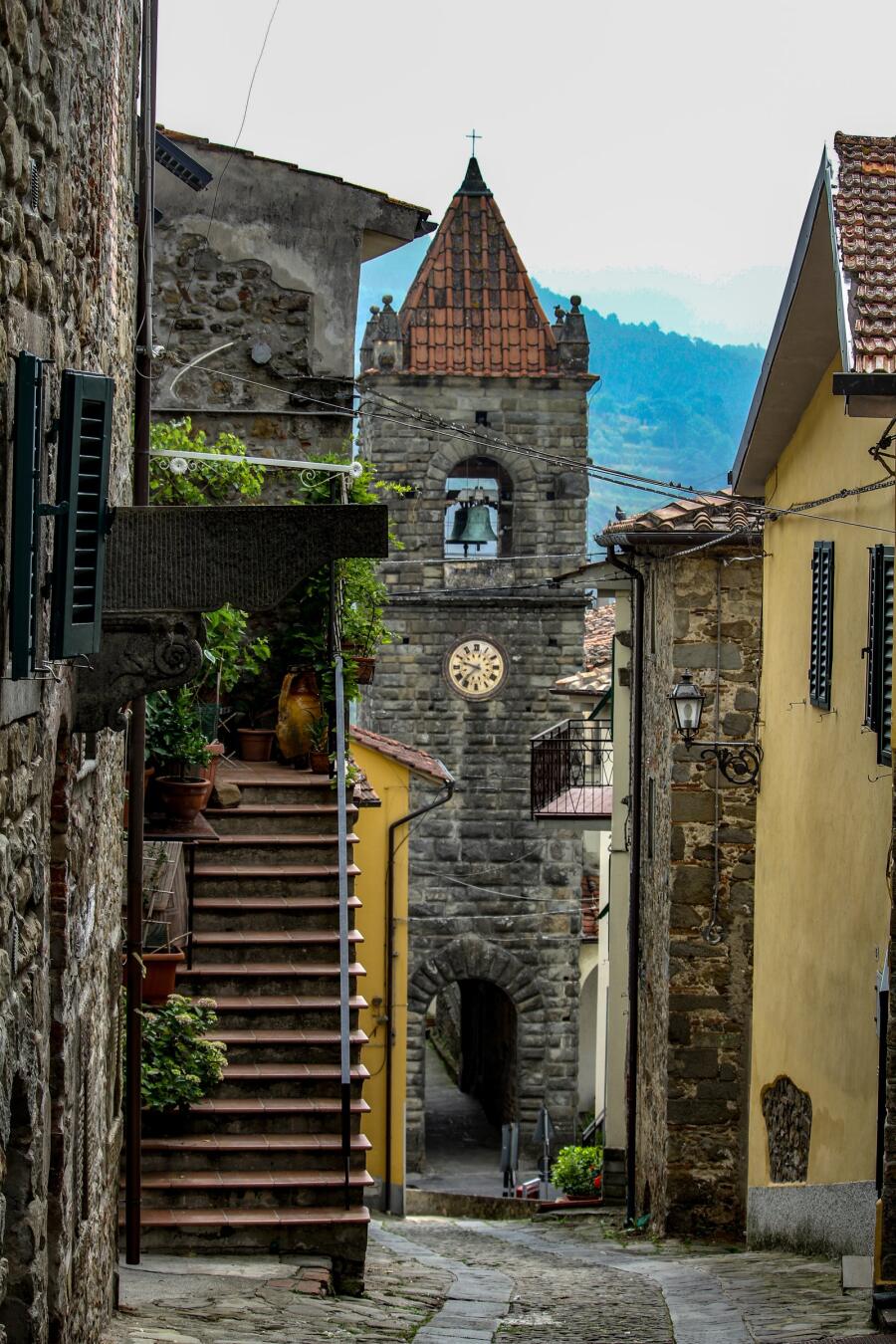 A stone staircase climbing between houses toward a bell tower with a pointed roof.