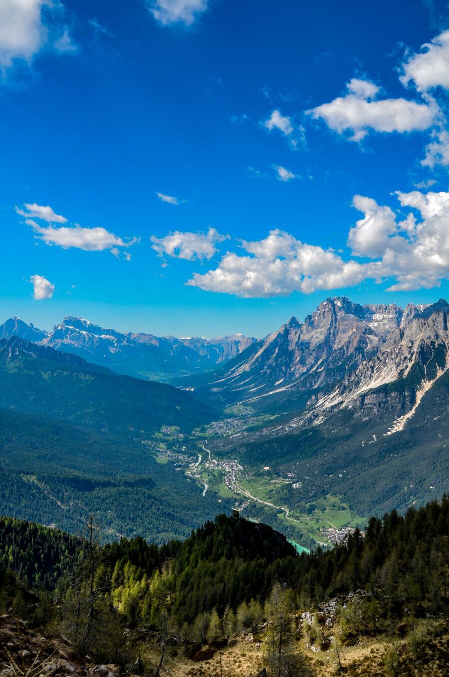 Looking down a forested valley toward distant peaks, with a village visible far below.
