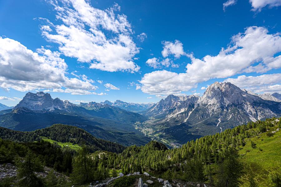 A broad green valley between rock massifs, under a deep blue sky filled with scattered cumulus.